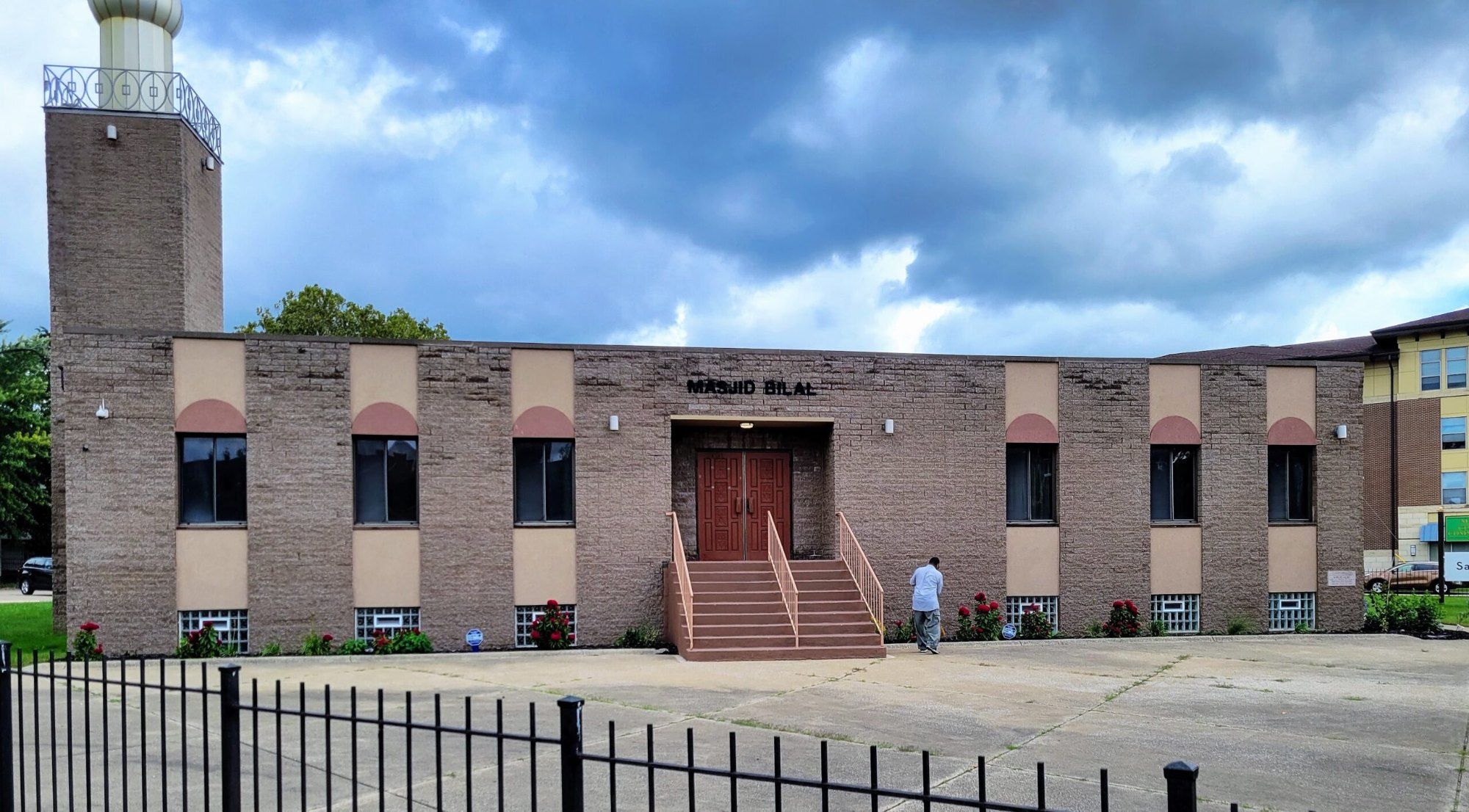 The front of Masjid Bilal on Euclid Avenue: a long brick building with arched panels over the windows, red front doors up a flight of steps, and the minaret at the left corner.