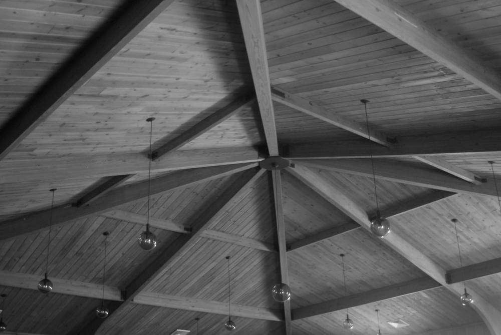 The timber roof beams of the musala, meeting at a central iron hub, with globe lamps hanging on long cords.