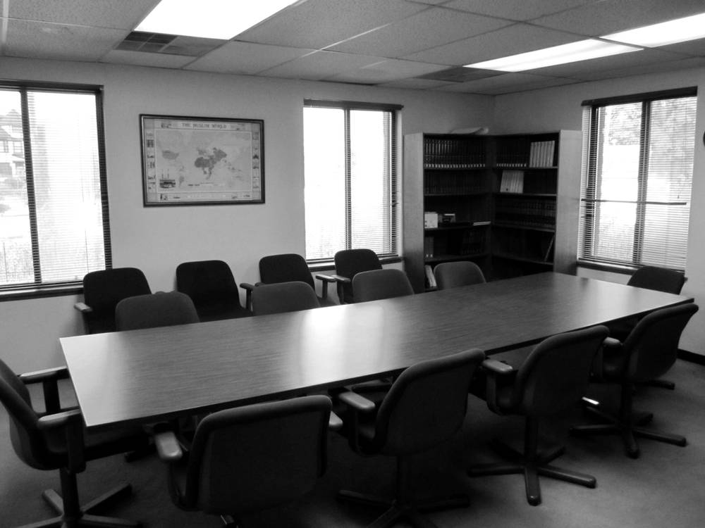 The masjid library: a long conference table with upholstered chairs, bookshelves in the corner, and a framed map of the Muslim world on the wall.