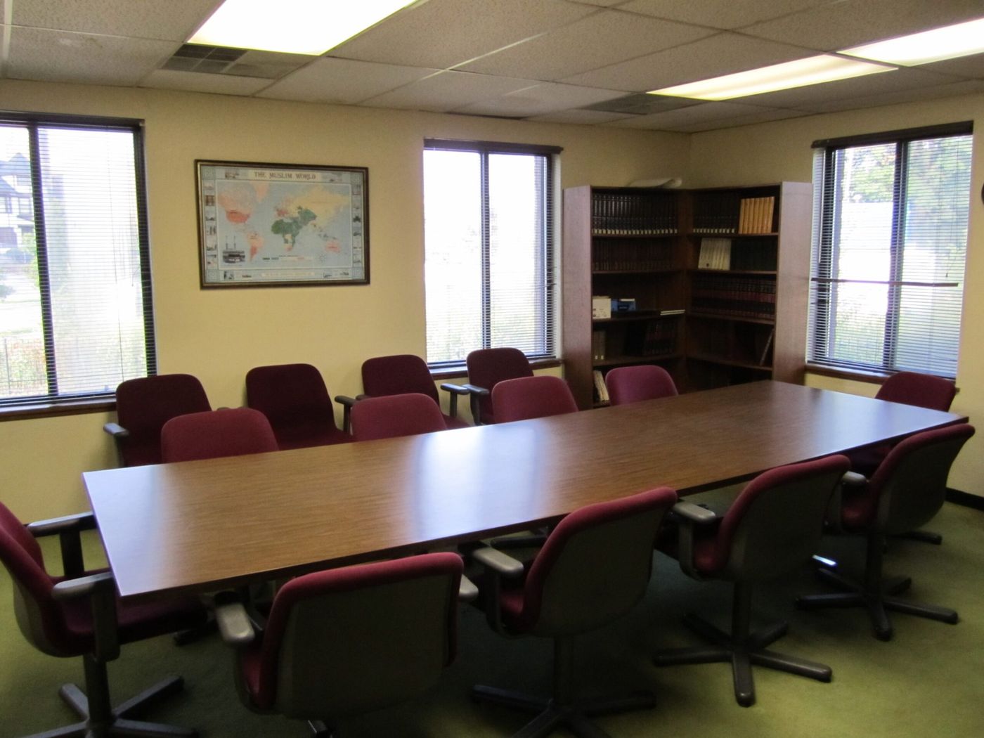 The masjid library: a long conference table with upholstered chairs, bookshelves in the corner, and a framed map of the Muslim world on the wall.
